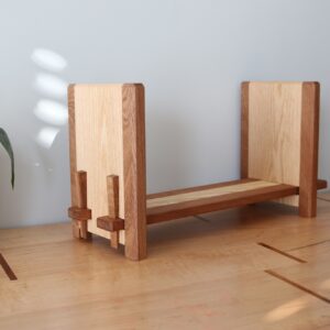 a wooden tabletop bookshelf with a plant on the left side of it and a candle on the right