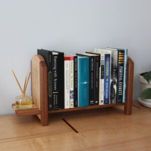 tabletop bookshelf with books on it with a ledge on the end holding a reed diffuser